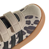 Close-up of a low-top sneaker showing the side panel with a beige and dark gray animal print, beige suede-like overlays with hook-and-loop straps, black side stripes, and a gum brown sole on a white background.