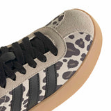 Close-up of a low-top sneaker showing the side panel with a beige and dark gray leopard print, black laces, a light gray suede overlay, and a gum-colored rubber sole on a white background.