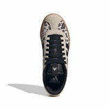 A single Adidas sneaker shown from a top-down view on a white background. The shoe features a light beige suede upper with black leopard print spots, black laces, a black collar, and a brown gum outsole.
