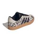 A low-top sneaker featuring a black and white leopard print pattern on the upper, black three-stripes, black laces, a black collar, and a brown gum sole, shown from a three-quarters angle on a white background.